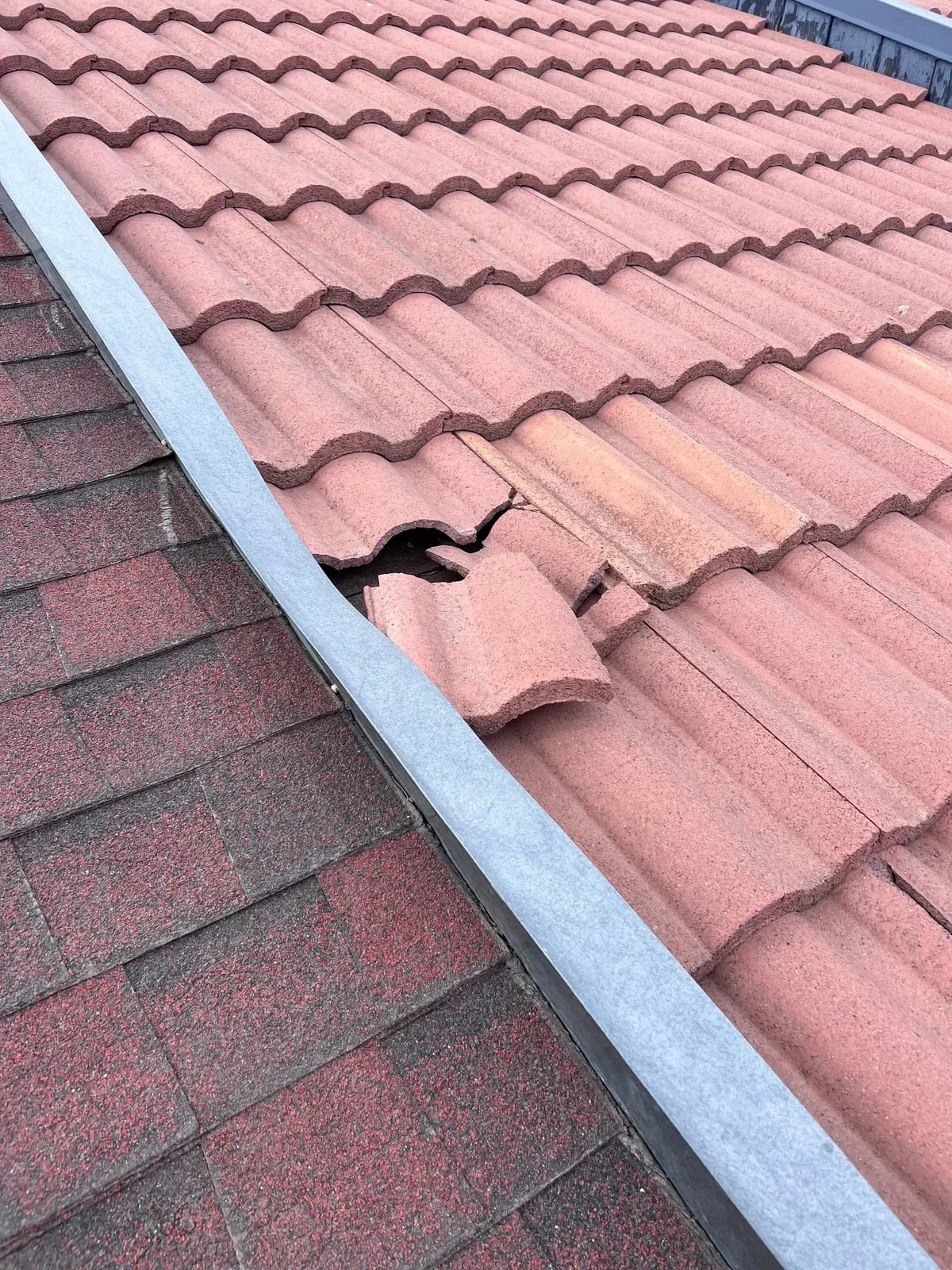 Broken red concrete barrel tile at a roof edge next to asphalt shingles