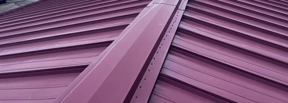 Burgundy standing seam metal roof panels meeting at the ridge cap