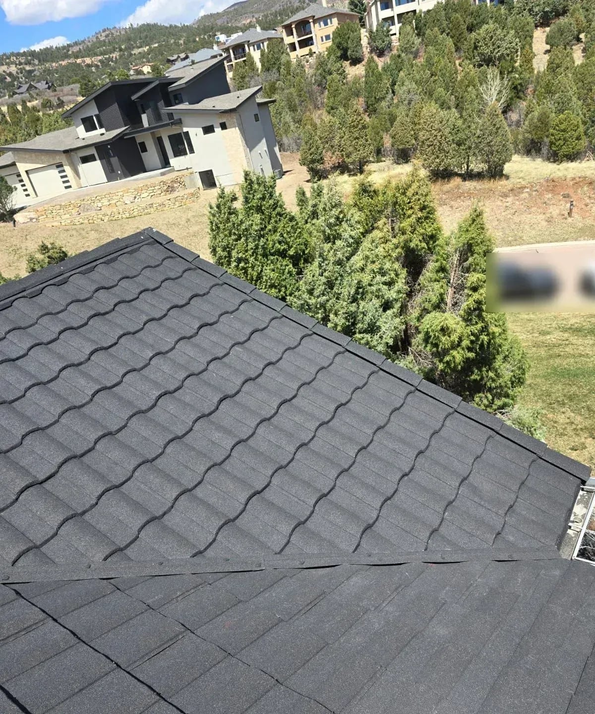 Charcoal stone-coated steel roof over a hip with a hillside neighborhood beyond