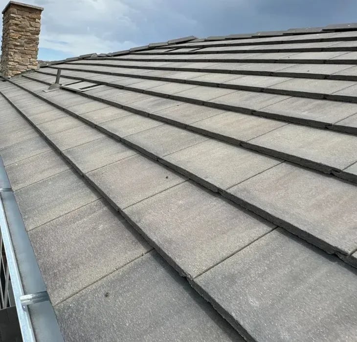 Gray flat concrete tile roof along a gutter line with a stone chimney