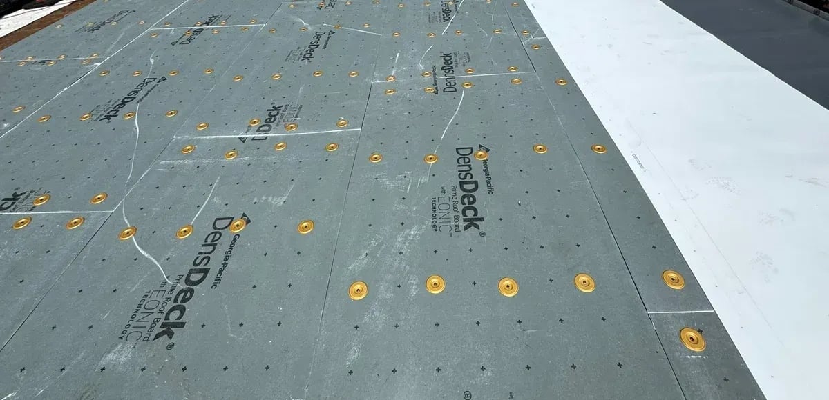 Gypsum cover board fastened with round plates next to a section of new white TPO membrane