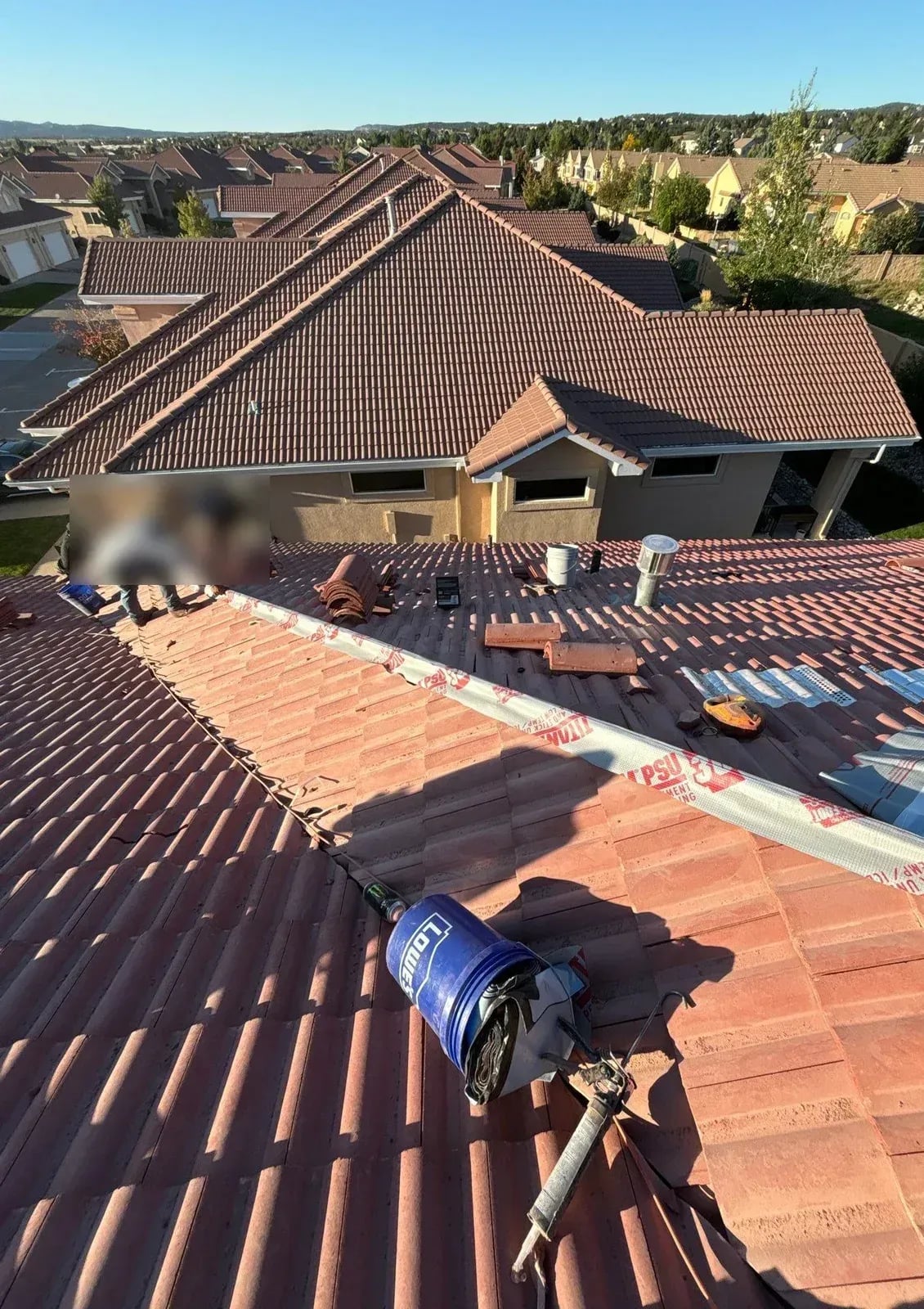 Roofer setting red tile courses on a sloped roof with neighboring tile roofs behind