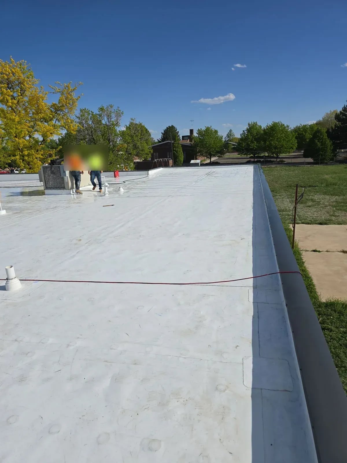 New white TPO membrane along a low-slope roof edge with a crew member working in the distance