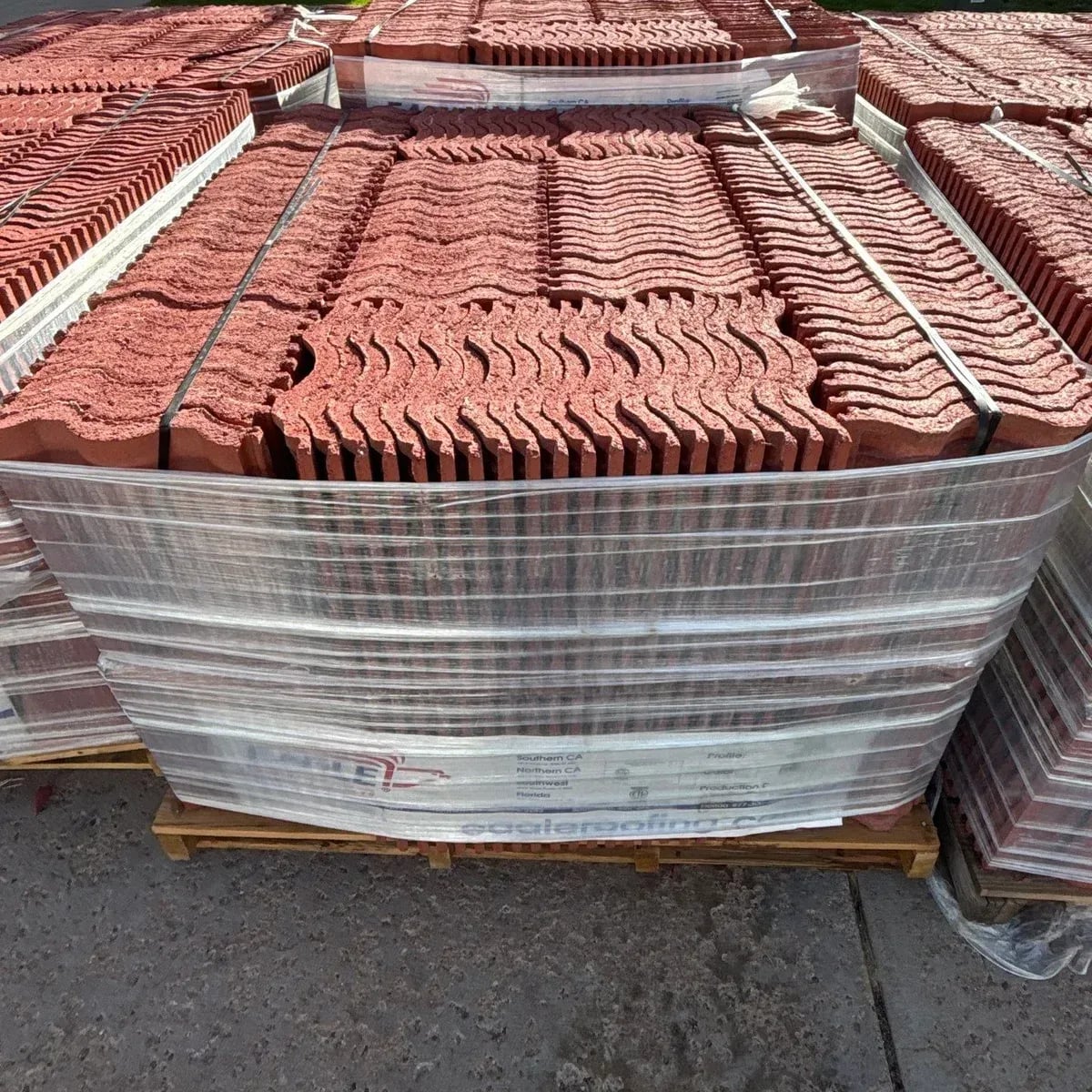 Pallets of new red concrete roof tile wrapped and staged on a driveway