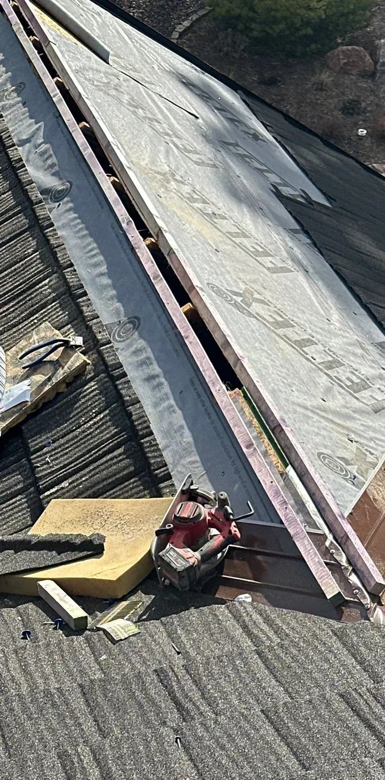 Stone-coated steel panels partly installed along a rake with trim stacked on the roof