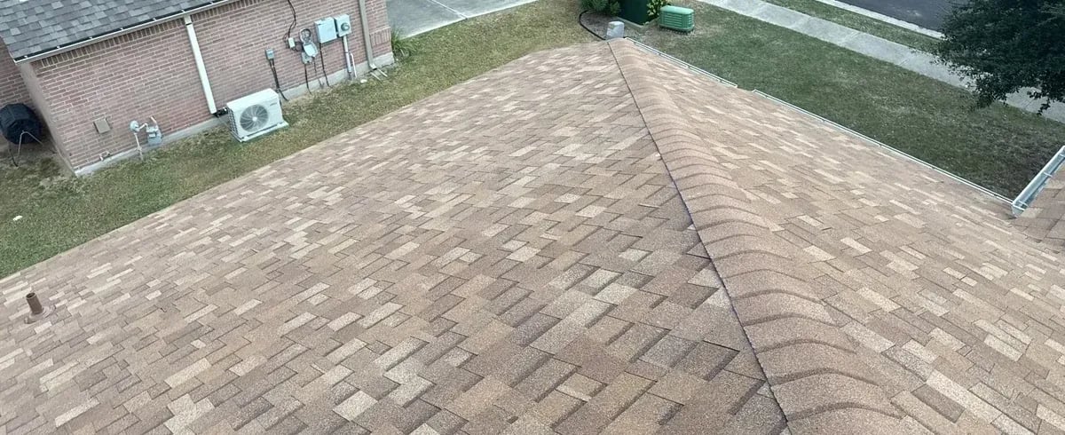 Brown-tan architectural shingles meeting at a hip with the yard and fence below