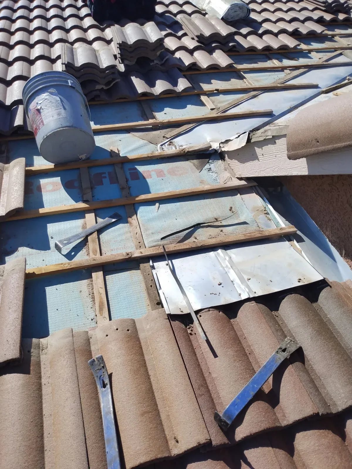 Concrete tile lifted to expose worn underlayment, battens and metal flashing
