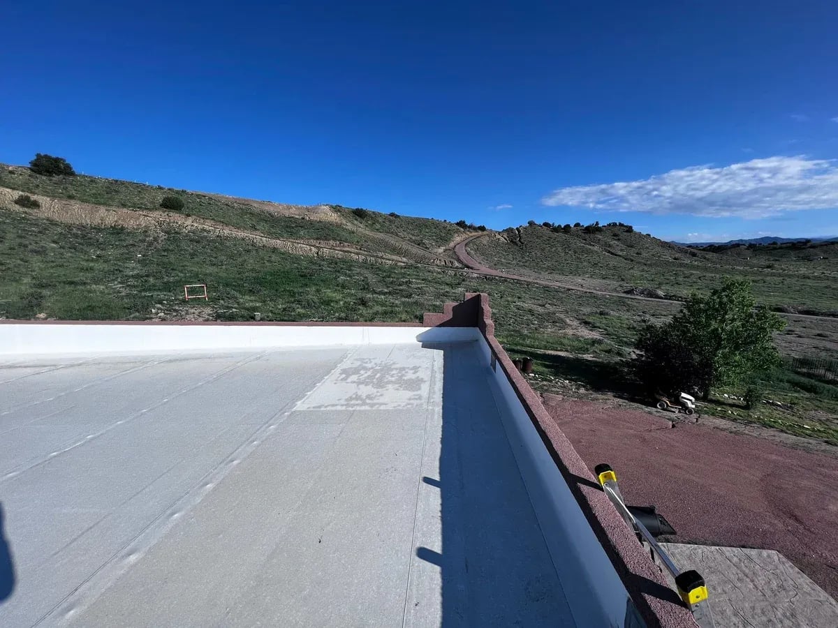 White TPO roof edge with metal edge flashing and a hillside beyond