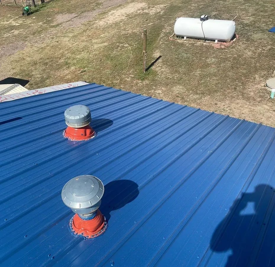 Two turbine vents with red flashing on a blue ribbed metal roof