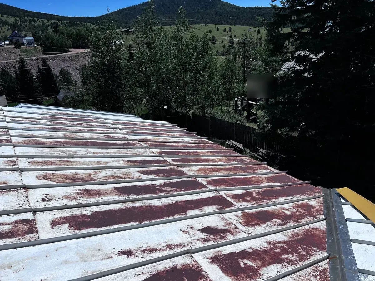 Old metal roof panels with peeling paint and rust, before replacement